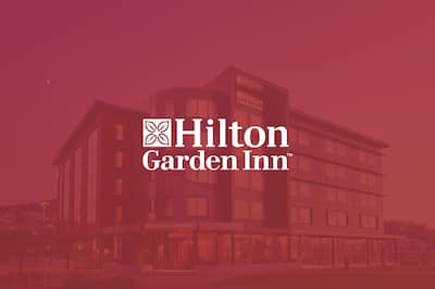 a hotel exterior with the Hilton Garden Inn logo layered over the top