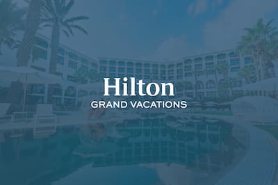 A hotel pool and exterior with the Hilton Grand Vacations logo layered over the top