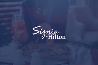 Woman holding fork and glass with the Signia by Hilton logo over the top of the image