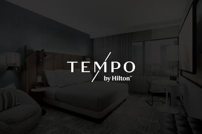 A hotel bedroom with the Tempo logo featured over the top of the image