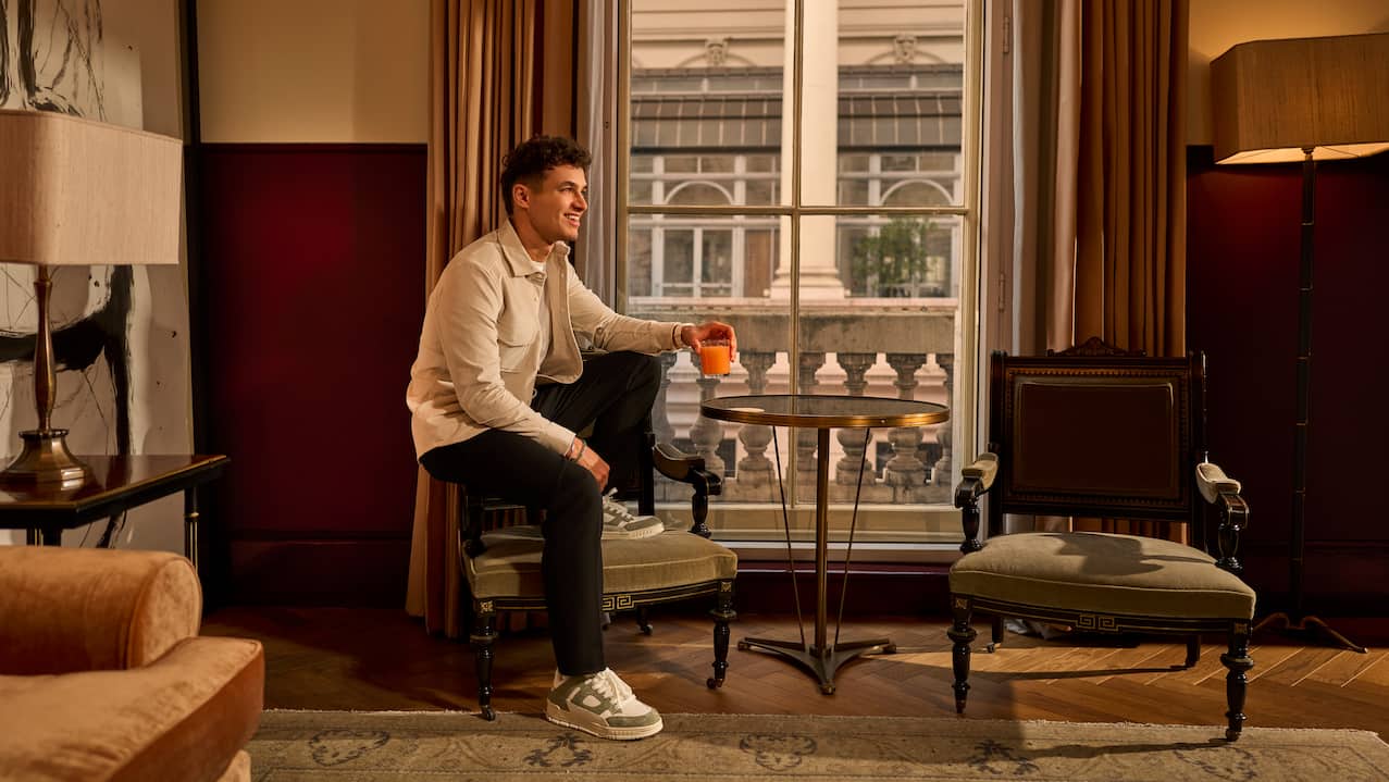 Lando Norris sitting on arm of chair holding orange drink