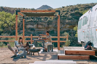 Woman reading a book outside in a chair and man pouring coffee
