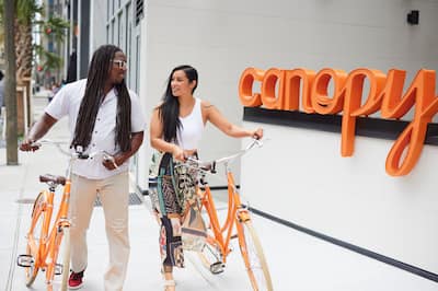 a couple holding bicycles in front of a Canopy hotel