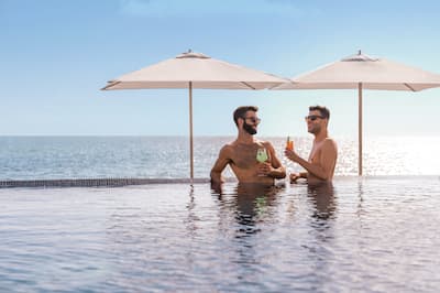 Two men stand in pool with drinks in hand