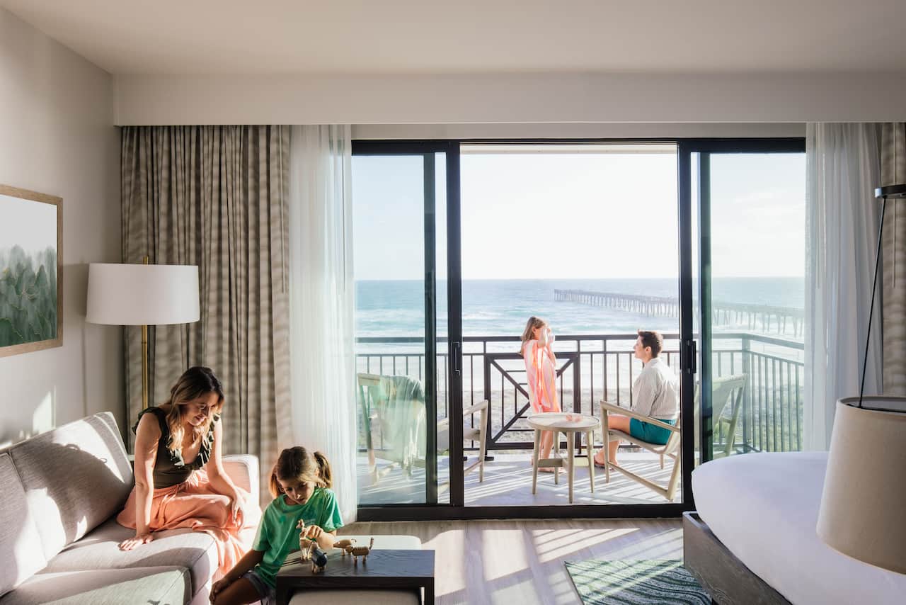 Women and daughter relaxing in a modern suite with father and daughter relaxing on the balcony with a sea view.