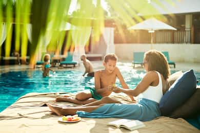 Woman and young boy relaxing by pool while people play in background