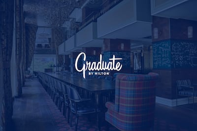 Lobby of a Graduate by Hilton hotel with a blue overlay and the Graduate by Hilton logo prominently displayed