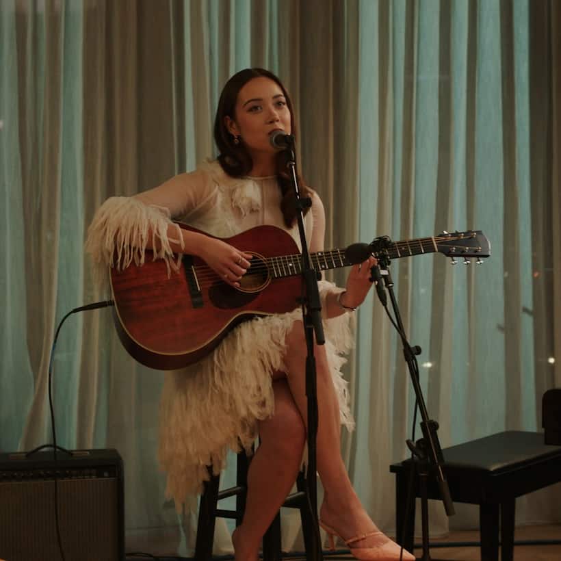 Musician Laufey sitting on a stool playing a guitar and singing into a microphone
