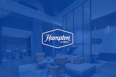 Hampton by Hilton hotel lobby with a blue overlay and white Hampton by Hilton logo displayed