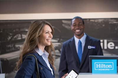 Woman holding cell phone showing room options with front desk reception team member in background