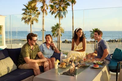 Group of friends relaxing in outdoor seating area. Food and drinks are on the table