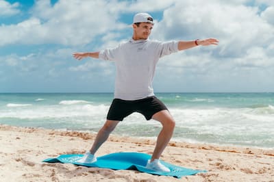 Lando Norris in a yoga pose on the beach with the ocean behind him
